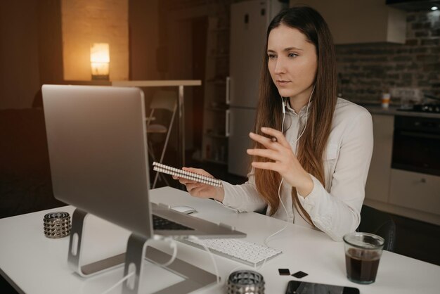 A caucasian woman with headphones working remotely on her laptop at home