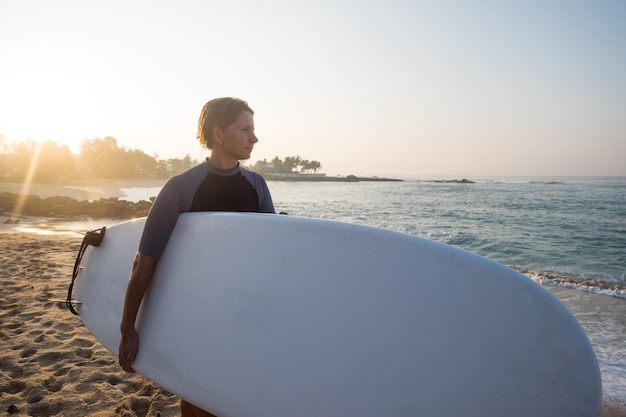 Caucasian woman with surfboard standing near water and looking at waves