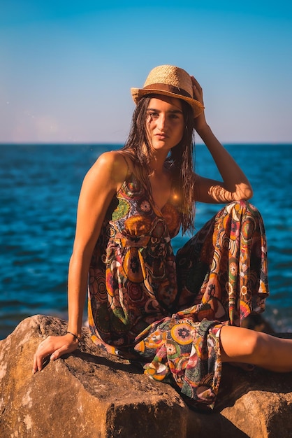 Caucasian woman with wet hair and a floral dress and a straw hat by the sea