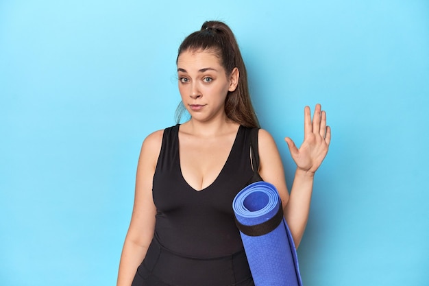 Photo caucasian woman with yoga mat in blue studio smiling cheerful showing number five with fingers