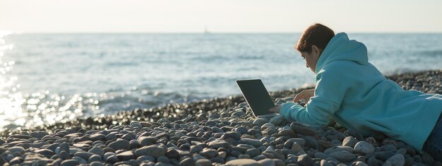 写真 白人の女性が石の砂浜でラップトップで働いています