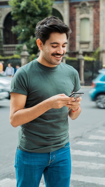 Caucasian young adult with cell phone in hands on the streets sending messages.