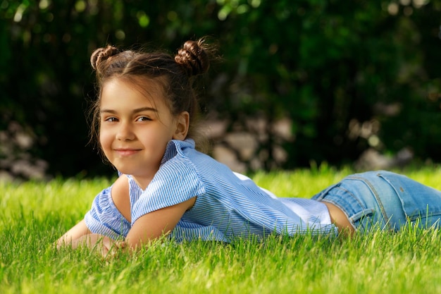 Caucasian young brunette girl lies on the grass in the park and smiles