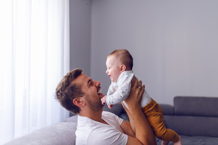 Photo caucasian young dad lifting his loving baby boy while sitting on sofa in living room