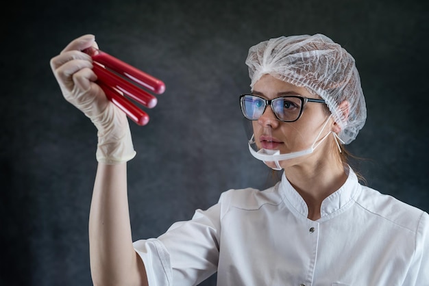 Photo caucasian young doctor in white coat looking a test tube with blood sample isolated on black