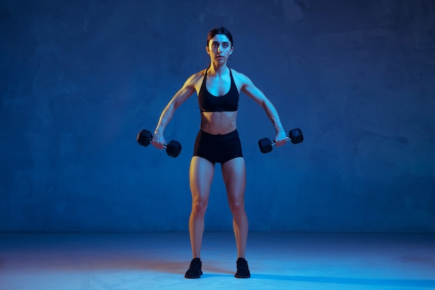 Caucasian young female athlete practicing on blue in neon light