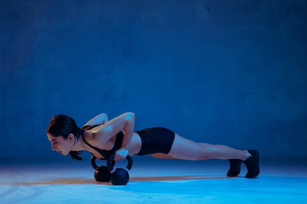 Caucasian young female athlete practicing on blue studio background in neon light