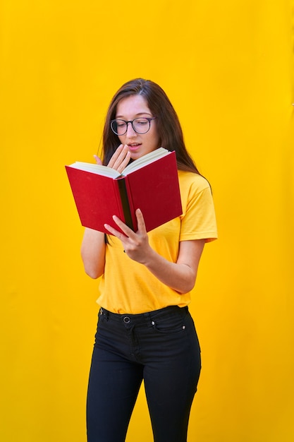 Caucasian young girl with long brunette hair reading a red book with surprised expression