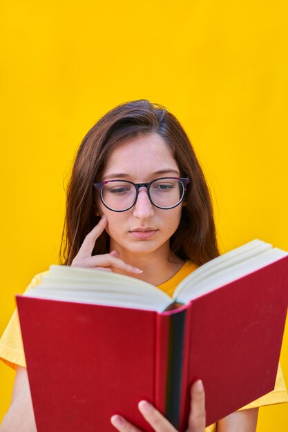 Ragazza giovane caucasica con capelli lunghi del brunette che legge un libro rosso