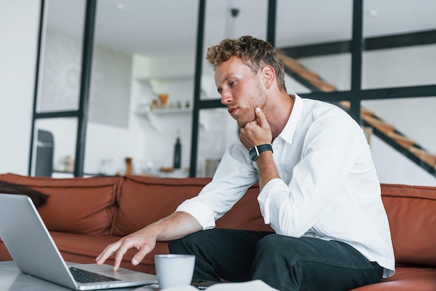 Caucasian young guy in elegant white shirt indoors at home