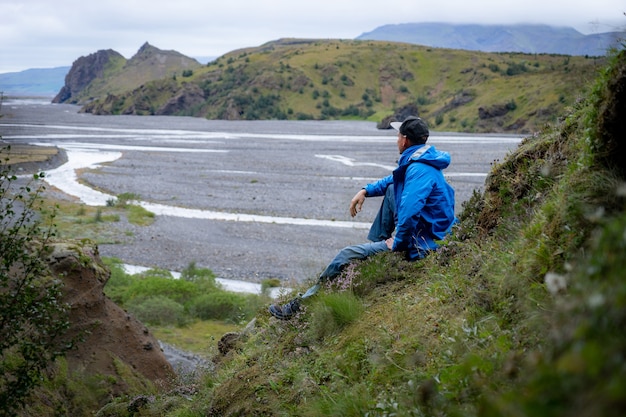 アイスランドのロイガヴェーグルトレイルの途中で山と峡谷の上に座っている白人の若い男。