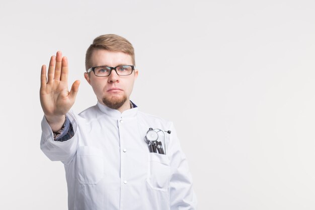 Caucasian young male doctor with stop gesture in white with copy space