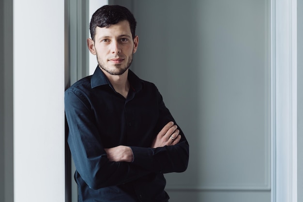 Caucasian young man portrait holding arms crossed, wearing black shirt on light background