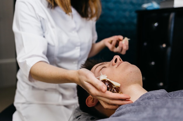 Caucasian young man receiving snails massage Face skin therapy and care with snails in spa salon Modern cosmetological procedure of skin rejuvenation