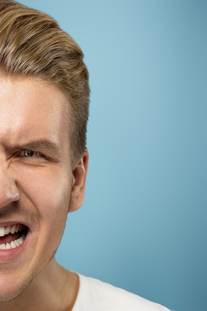 Caucasian young man's close up portrait on blue studio wall