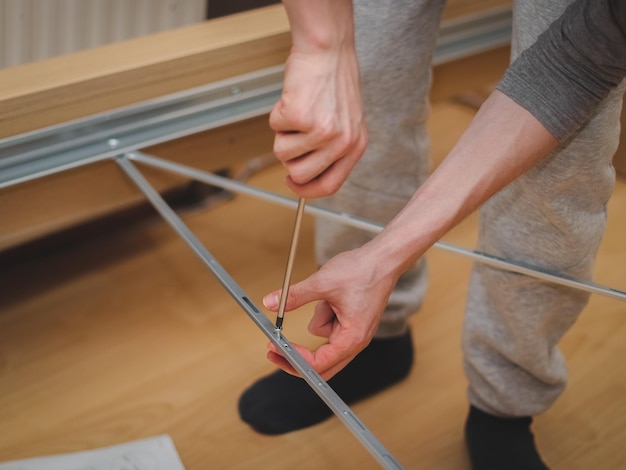 A caucasian young man a screw with a screwdriver connecting metal parts to a bed