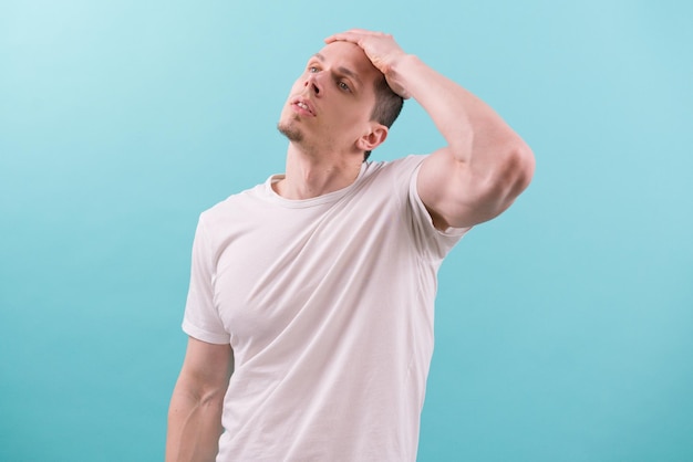 A caucasian young man in white  holds his hand to his head and stares up  a light blue Depress Hard