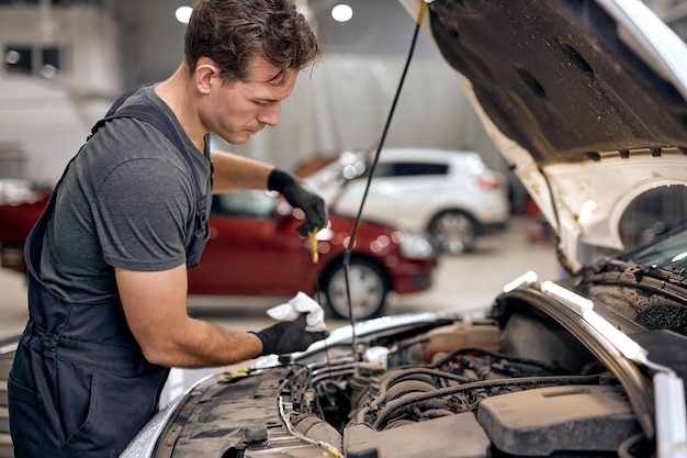 Photo caucasian young mechanic in uniform doing car service and maintenance oil and fuel filter changing m...