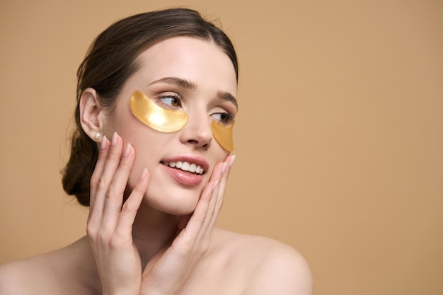 Caucasian young pretty woman applying golden collagen patches under her eye