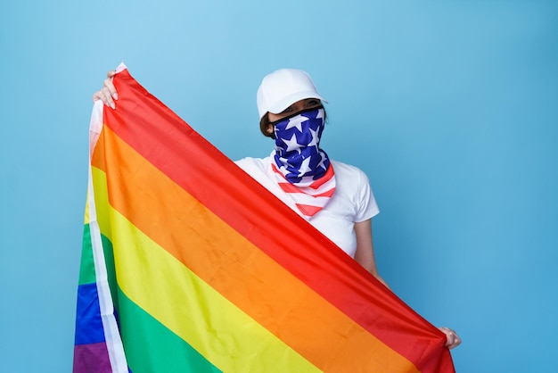 青色の背景に虹色の旗でポーズをとる白人の若い女性