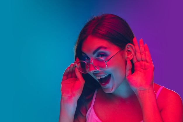 Caucasian young woman's portrait isolated on gradient purple-blue background in neon light, cinema, movie watching