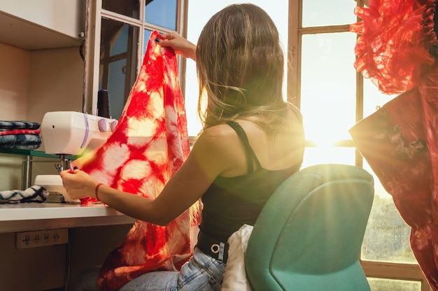 Caucasian young woman sitting in her workshop by the sunlit window holding a red cloth