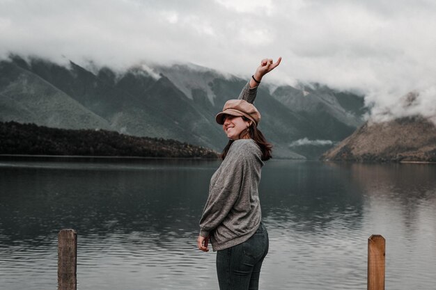 Photo caucasian young woman standing happy and content in gray shirt and brown beanie on her head smiling