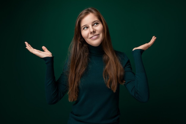 Caucasian young woman wearing a green turtleneck on a dark background with copy space