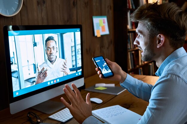 Foto caucasian zakenman financieel adviseur aandelenhandelaar makelaar consulting afrikaanse cliënt investeerder over investeringen op videoconferentie oproep virtuele externe vergadering chat met behulp van pc computer en telefoon app