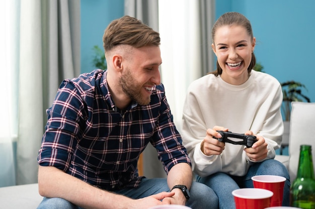 Cauciasian friends sitting at home on couch and playing video games on console