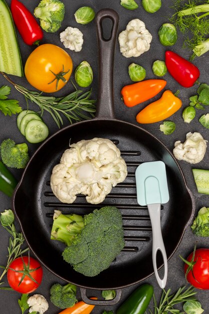 Cauliflower and broccoli in frying pan. Multicolored vegetables on table. Black background. Flat lay.