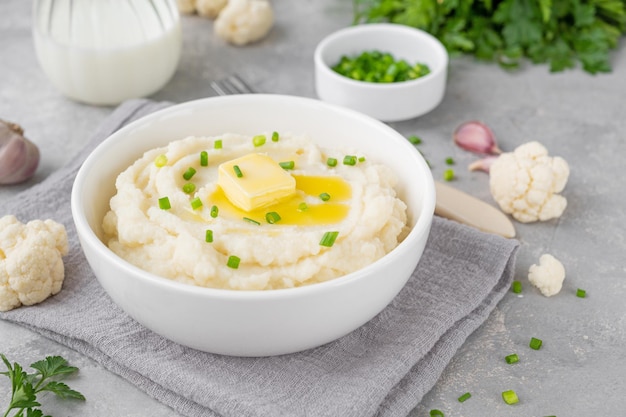 Cauliflower puree with butter and green onions in a white bowl on a gray concrete background