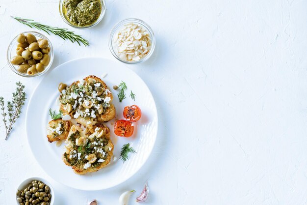 Cauliflower steak with spices chimichurri sauce almond flakes olives fried cherry tomatoes and capers on a white plate Vegetarian food White background Copyspace