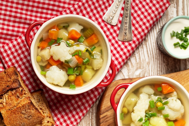 Photo cauliflower vegetables soup in bowl, bread, cream on wooden table