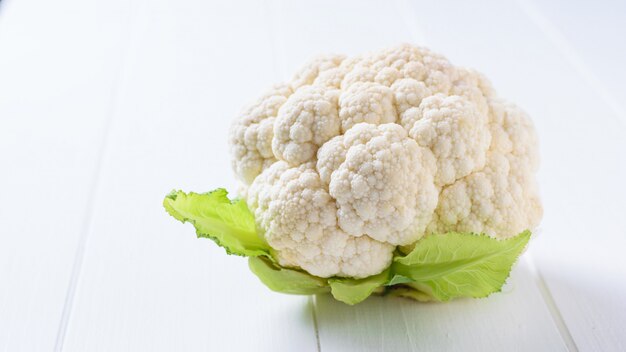 Cauliflower with leaves on a white wooden table.