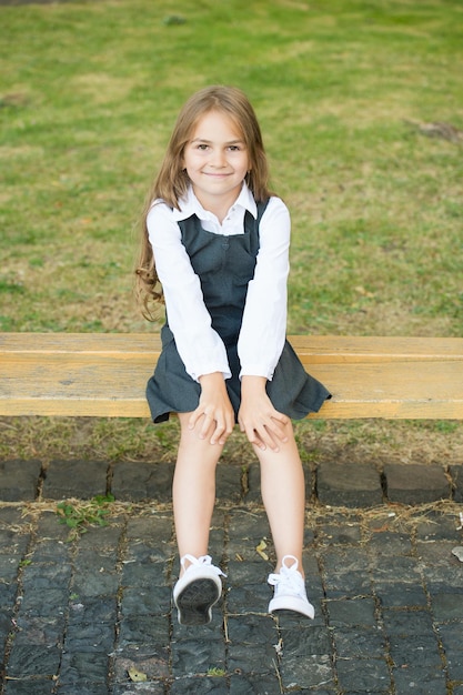 Cause your little one deserves it. Happy child sit on bench outdoors. School look of child girl. Formal fashion. Uniform dress. Primary education. Childcare and childhood. International childrens day.