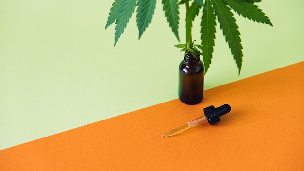 Cbd cannabidiol oil and cannabis leaves on minimal orange and green background cbd hemp oil in