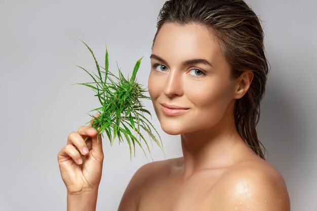 CBD cosmetica concept. Mooie vrouw met een cannabisblad op grijze achtergrond