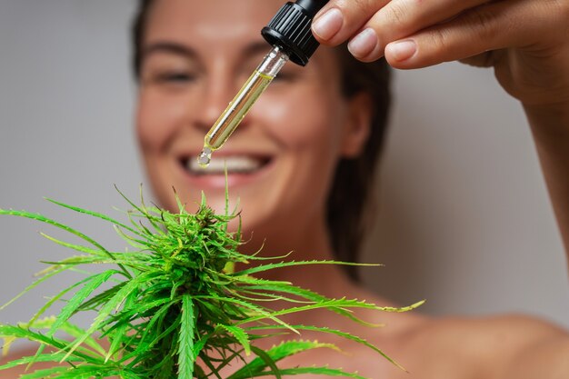 Foto concetto di cosmetici cbd. bella donna con una foglia di cannabis su sfondo grigio