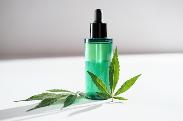 Cbd facial oil with cannabis extract for a natural skin\
treatment natural herbal cosmetic skin treatment concept marijuana\
leaves next to green bottle