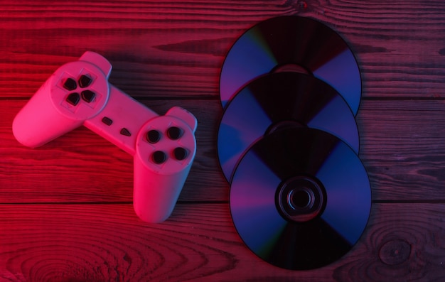 Cd-schijven, gamepad op houten oppervlak. Neon rood en blauw licht