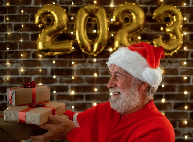 Celebrate event new year for caucasian bearded elderly male holding Christmas presents beautiful senior adult man in Santa hat celebrate holiday at home by night