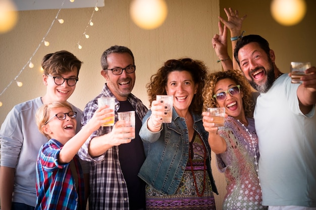 Festeggia il concetto di persone con età diverse, adulti e giovani che brindano tutti insieme divertendosi e ridendo molto - dal bambino all'adolescente fino agli uomini e alle donne adulti nella notte dell'evento della festa