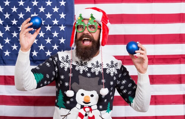 今日を祝います。アメリカ人男性は冬休みを祝います。星条旗の背景に愛国的なサンタ。クリスマスと新年をアメリカの方法で祝いましょう。季節のご挨拶。落ち着いて祝いましょう。