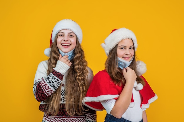 Celebrate winter holidays on quarantine. christmas shopping online. friendship of teen girls. sale for presents and gifts. happy santa claus children. smiling kids in santa hat and protective mask.