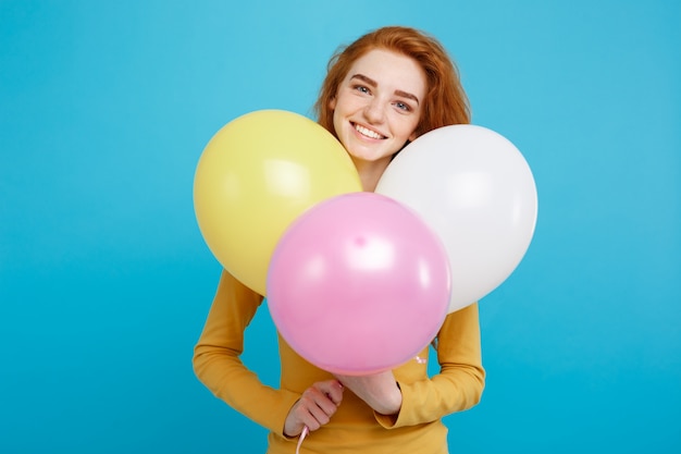 Celebrating Concept - Close up Portrait happy young beautiful attractive redhair girl smiling with colorful party balloon. Blue Pastel Background.