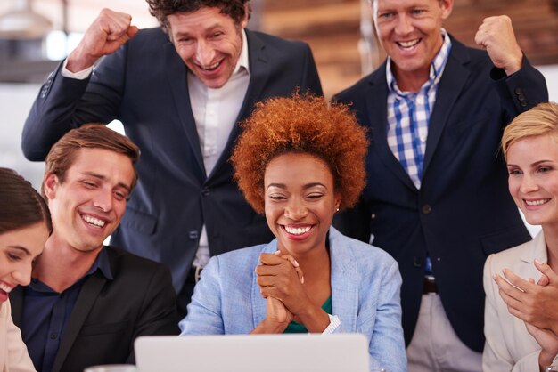 Photo celebrating the good news cropped shot of a group of businesspeople gathered around a single laptop