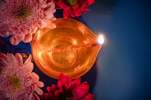 Celebrando il festival indiano della luce diwali primo piano delle tradizionali lampade a olio di diya e fiori su sfondo blu