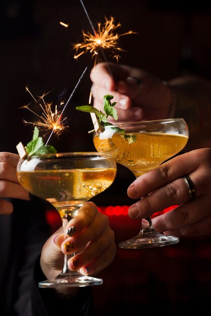 Celebrating new year eve 2022 with sparklers fireworks and drinking cocktails. Mint with orange slice in a cocktail glass filled with alcohol cocktails.