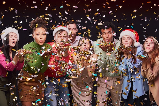 Celebrating new year  together group of young multiracial happy people blowing colorful confetti